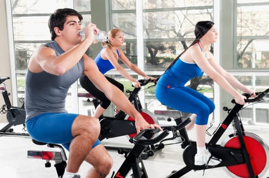 Man drinking water with two women working out in a gym