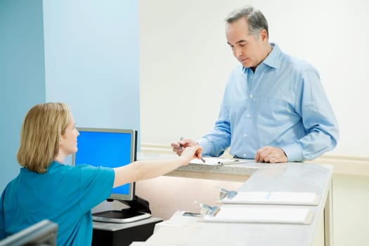 Female nurse helping a patient in filling form at a reception counter in a hospital