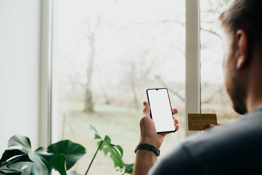 Man holds smartphone with white screen and bank card. High quality photo