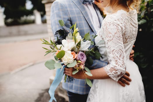 Bride in white dress is holding wedding bouquet. Groom hugs the bride. Blurred background. High quality photo