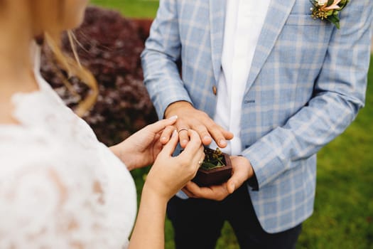 Bride puts wedding ring on groom finger. Boutonniere. Blurred background. High quality photo