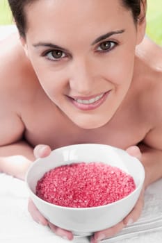 Portrait of a woman lying on a massage table and holding a bowl of bath salt