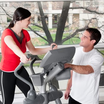 Woman working out on a stepping machine and talking to a man in a gym