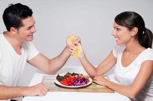 Couple squeezing oranges over vegetable salad