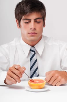 Close_up of a businessman eating a grapefruit with a spoon