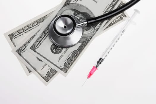 Close_up of hundred dollar bills with a stethoscope and a syringe