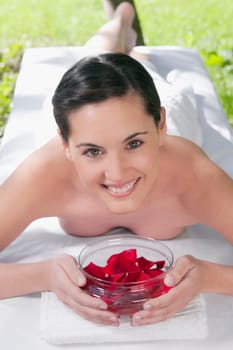Portrait of a woman lying on a massage table holding a bowl of rose petals