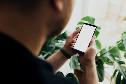Man is holding smartphone with white screen. Blurred background. High quality photo