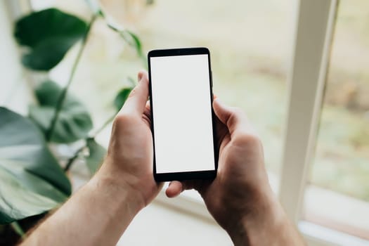 Man is holding smartphone with white screen. Blurred background. High quality photo