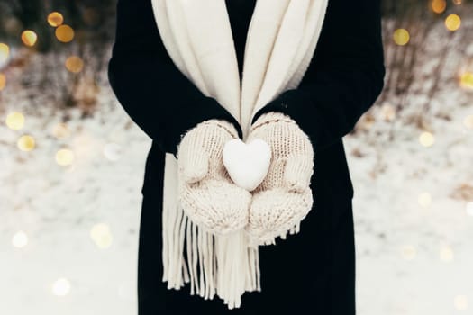 Snow heart snowball in girl gloved hands. Blurred background. High quality photo