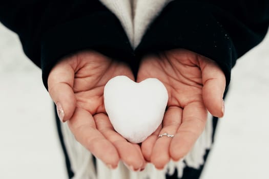 Snow heart snowball in girl gloved hands. Blurred background. High quality photo