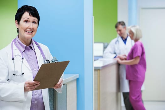 Female doctor holding a clipboard with a doctor and nurse in the background