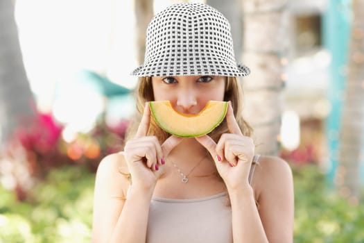Woman holding a slice of melon in front of her mouth