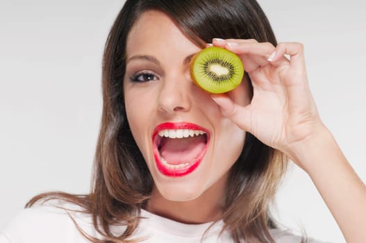 Woman holding half a kiwi over her eye