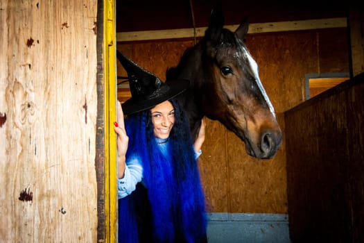 A girl dressed as a witch holds a horse in a paddock