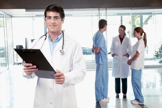 Doctor holding a clipboard with his colleagues discussing in the background
