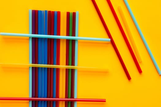 Multi-colored cocktail tubes lie on a yellow background
