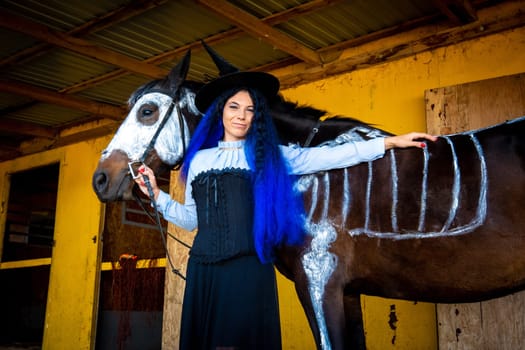 Halloween celebration, a young girl in a witch costume stands by a horse with a skeleton drawn
