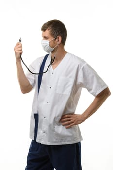 Doctor in a mask looks at a phonendoscope dressed on himself