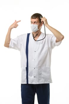 Masked doctor using a phonendoscope listens to his head, with the other hand making a pistol gesture points to his head, isolated on white background