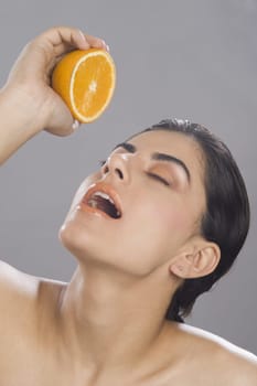 Close_up of a woman squeezing juice from a half of orange in her mouth