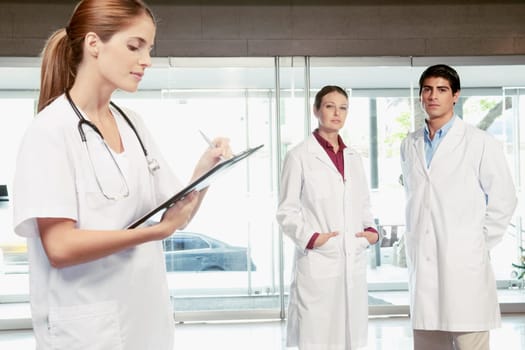 Female nurse writing on a clipboard with her colleagues standing in the background