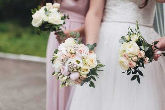 Bride in white dress is holding wedding bouquet with bridesmaids. Blurred background. High quality photo