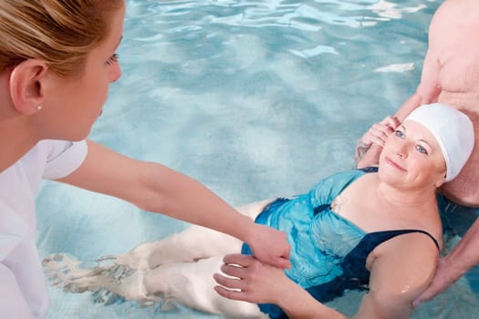 Health worker and a man assisting a woman in a swimming pool