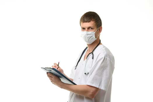 A male doctor writes in a clipboard with a ballpoint pen and looked into the frame