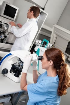 Female lab technician analyzing a sample through a microscope