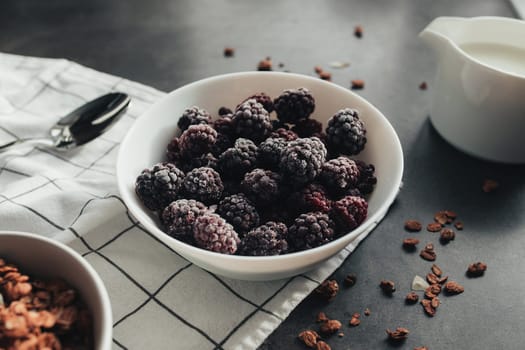 Frozen blackberries, granola, cream, towel on table. Blurred background. High quality photo