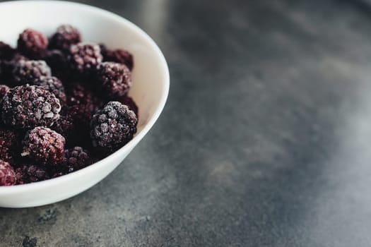 Frozen blackberries in a bowl on the table. Blurred background. High quality photo