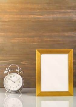 Picture mock up with golden frame and alarm clock over table with wood wall background