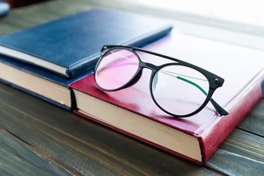 Reading glasses put on hardcover books over wooden table