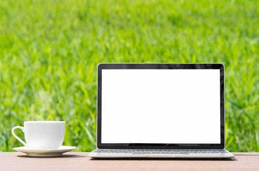 laptop and cofree cup on wood plank agent green grass field in countryside