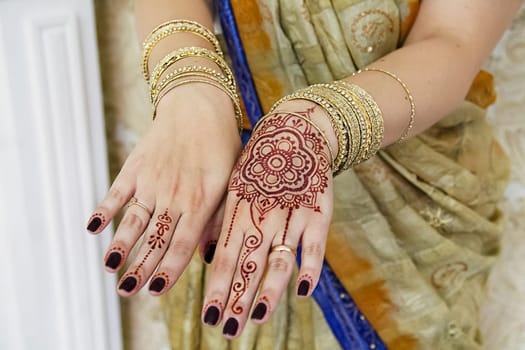 Indian woman's hands in gold bracelets and tattoos.