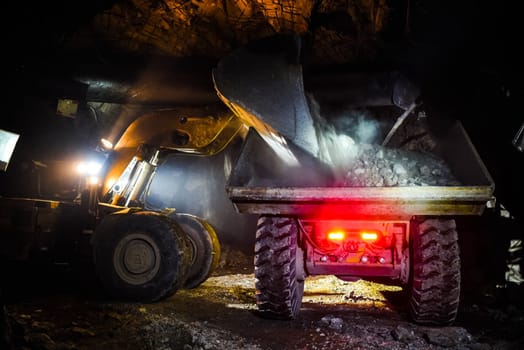 Loading the rock with a bulldozer into a dump truck. Work in the mine.