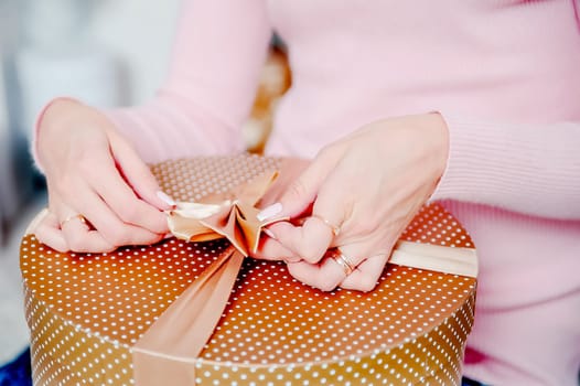 A woman ties a box with a gift. Gift packaging.