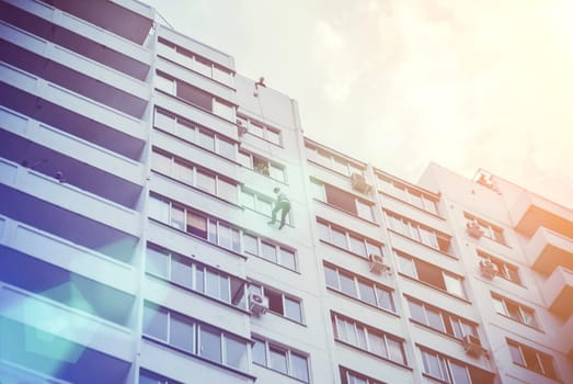 A man on a rope descends from the roof of a building on a rope through a window.