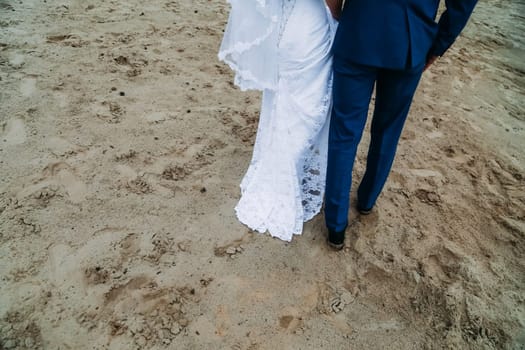 The bride and groom are walking on the sand. Walking along the shore