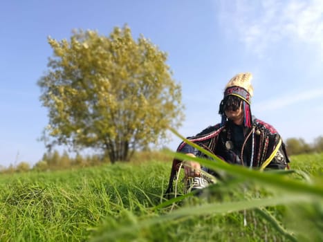 A young shaman sits on a lawn near a tree.