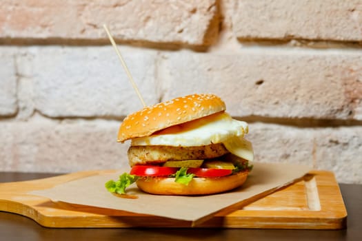 A hamburger on a wooden board with a wooden stick stuck in it.