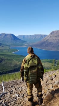 A tourist traveler stands with a backpack over a mountain valley.