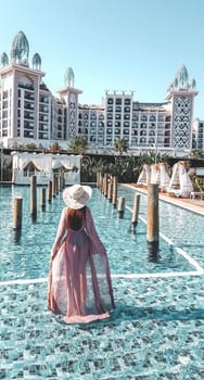 A girl walks around the pool in a dress. small pool near the hotel.