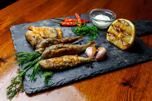 Fried fish on a chopping board with dill lemon garlic and salt.