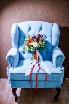 A beautiful bouquet of the bride lies on a blue chair.