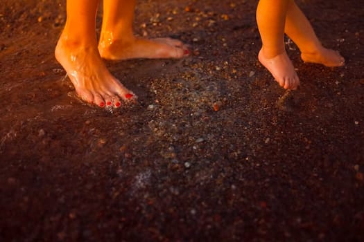 The legs of the baby and mother on the beach. Swimming in the sea with a child.