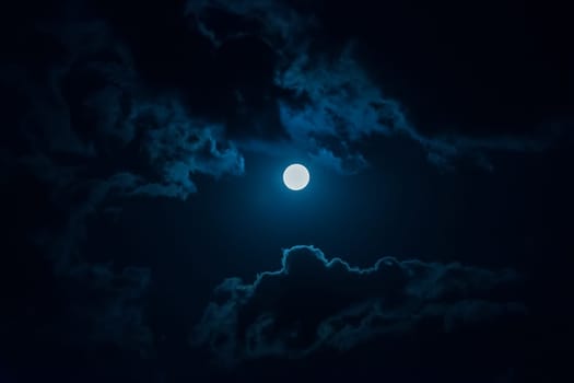 A full moon in the night sky among the clouds.