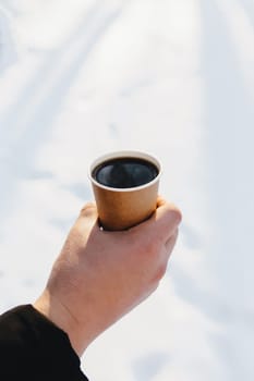 Guy holds paper cup of coffee in hand in the snowy forest. Blurred background. High quality photo
