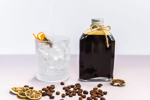 Cold brew coffee in a bottle with transparent glass full of ice on light gray background